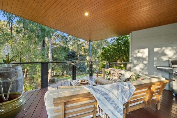 Aroha Studio covered verandah with cushioned timber lounge chairs, timber floor and railing, gas BBQ and leafy bushland outlook, Margaret River