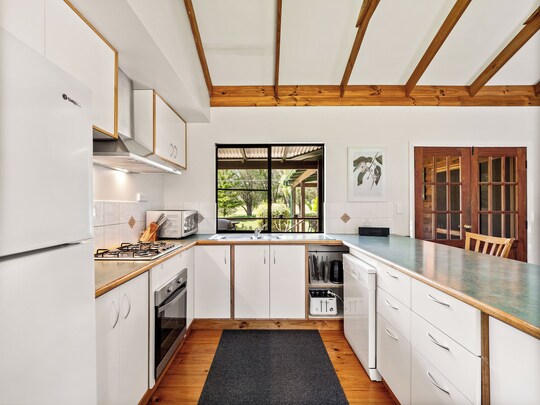 Brumby Cottage kitchen with white cabinets, timber beams, fridge, microwave, oven and gas cooktop, window to verandah, Margaret River