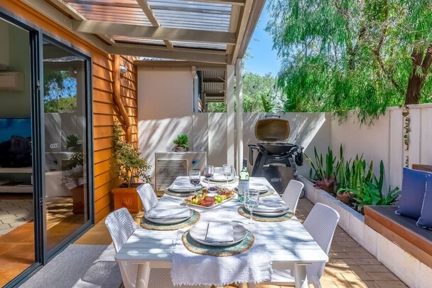 Aroha Studio covered verandah with cushioned timber lounge chairs, timber floor and railing, gas BBQ and leafy bushland outlook, Margaret River